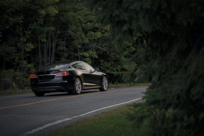 Side view of car driving down the road with a forest on either side.